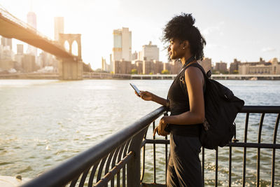 Usa, new york city, brooklyn, woman with cell phone standing at the waterfront