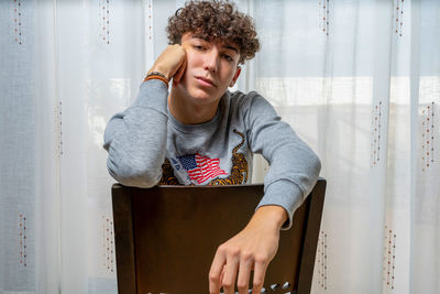 Portrait of young man siting against curtain