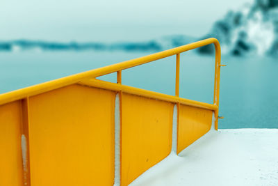Close-up of yellow railing at beach against sky