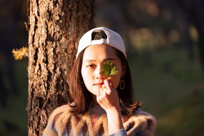 Portrait of young woman against tree trunk