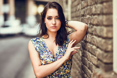 Portrait of young woman standing against brick wall