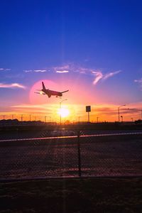 Silhouette airplane flying against sky during sunset