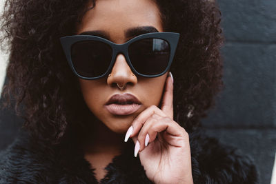 Portrait of woman in sunglasses and fur coat against wall