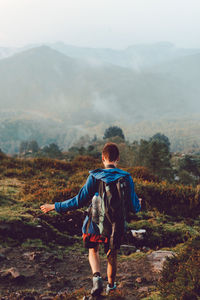 Back view of active touristic person in blue jacket and backpack climbing on ill with dry orange vegetation in spain