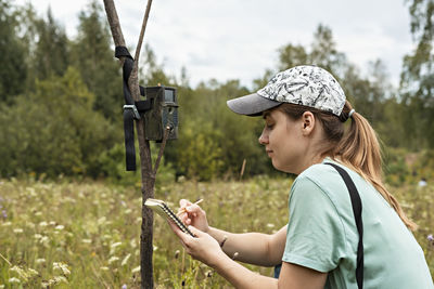 Side view of woman holding hat on field