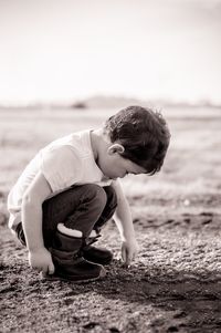 Full length of boy crouching at sandy beach