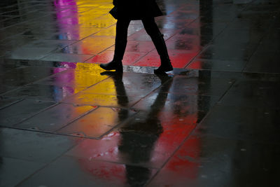 Low section of woman walking on wet footpath in city at night