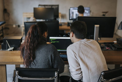 Rear view of young male and female colleagues coding together on laptop at startup company