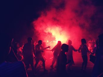 People dancing around bonfire on street at night during festival