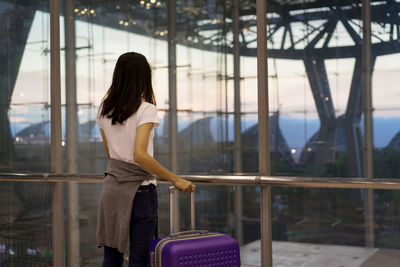 Rear view of woman standing by railing against window