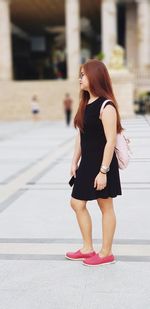 Full length of woman standing on sidewalk in city