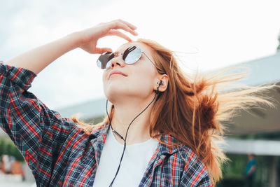 Beautiful young woman listening music against sky