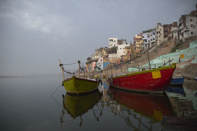 Fishing boats moored on sea by buildings against sky