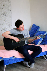 Young man playing guitar against wall