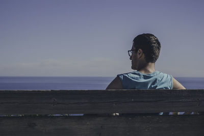 Man sitting by sea against clear sky