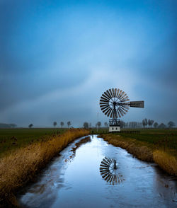 Traditional windmill by lake against sky