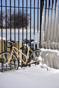 Bicycle by snow covered fence