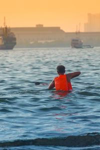 Rear view of man in sea against sky during sunset