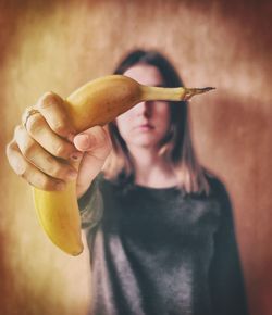 Woman holding banana while standing against wall