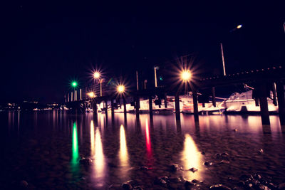 Illuminated street lights by river against sky at night