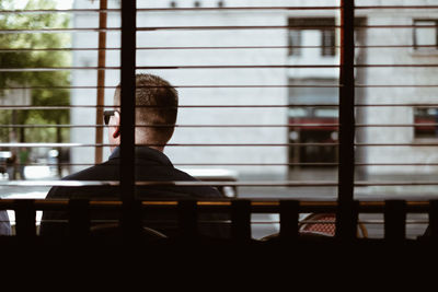 Rear view of man sitting on chair seen through window