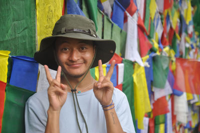 A asian young guy looking at camera with making peace sign, posing against tibetan prayer flags