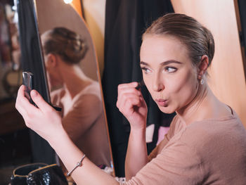 Side view of young woman applying make-up while sitting at home