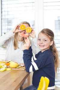 Portrait of girl with mother holding orange fruit at home