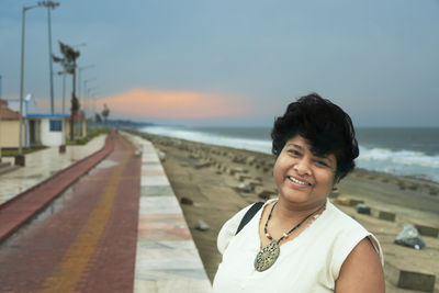 Portrait of smiling woman standing at beach against sky