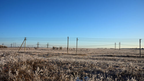 Electricity pylon on field against clear blue sky