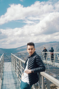 Portrait of young man standing on railing against sea