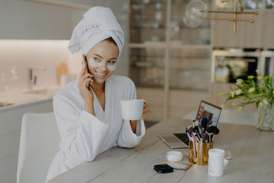 Smiling woman with eye patch talking on phone while holding coffee cup at home