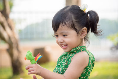 Smiling girl holding toy in finger against trees