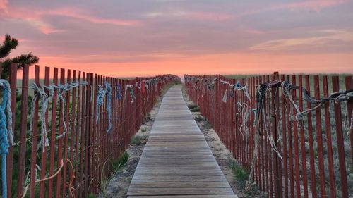 Empty wooden boardwalk leading towards sky during sunset