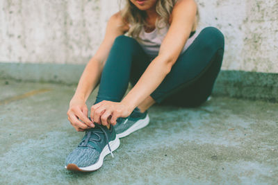 Low section of woman tying shoelace on footpath