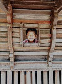 Portrait of boy looking through wooden window