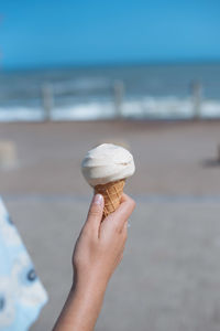Cropped hand holding ice cream cone at beach