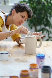 Craftswoman at work scraping and shaping clay pottery jug with professional tool in artistic studio