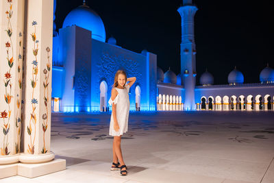 Woman standing by illuminated building at night