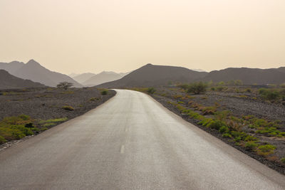 Empty road leading towards mountains against clear sky