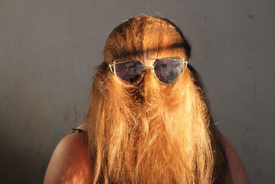 Close-up portrait of woman wearing sunglasses against wall