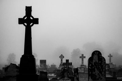 Cross in cemetery against sky