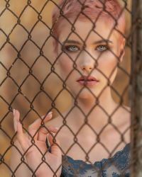 Portrait of young woman seen through chainlink fence