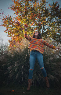 Full length of woman standing by tree in autumn