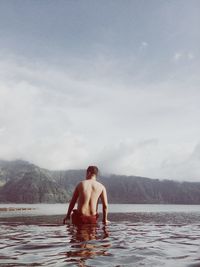 Rear view of shirtless man in water against sky