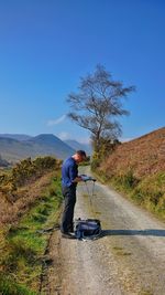 Man reading book on road against sky