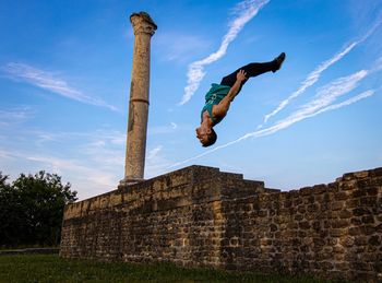 Low angle view of man jumping against wall and sky