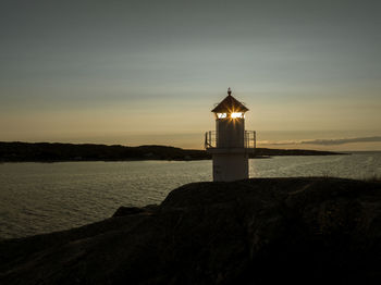 Lighthouse by sea against sky during sunset