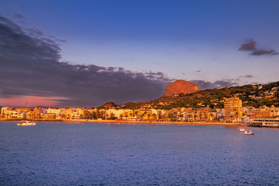 City by sea against sky at sunset
