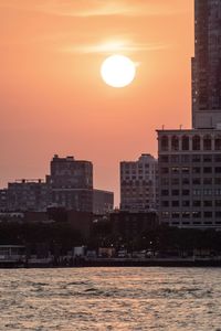 Sea by buildings against sky during sunset